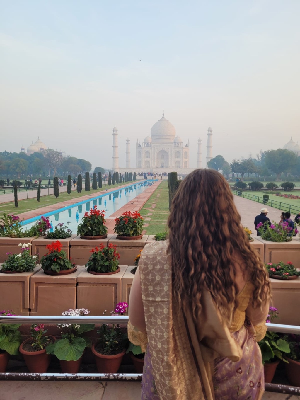 Image of me in a purple and gold saree stood facing the Taj Mahal in the background