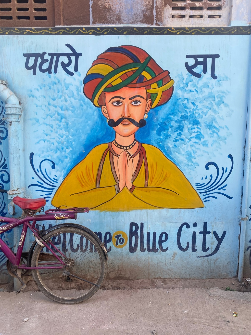 Image of wall painted with praying man wearing turban, underneath is written 'welcome to the blue city'